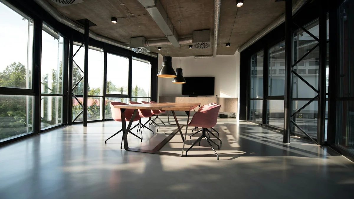 A bright modern meeting room with a wooden table, pink chairs, tall windows and pendant lights - a Quiet Core Reset guide to Why Perfect Routines Are the Enemy of Good Ones.