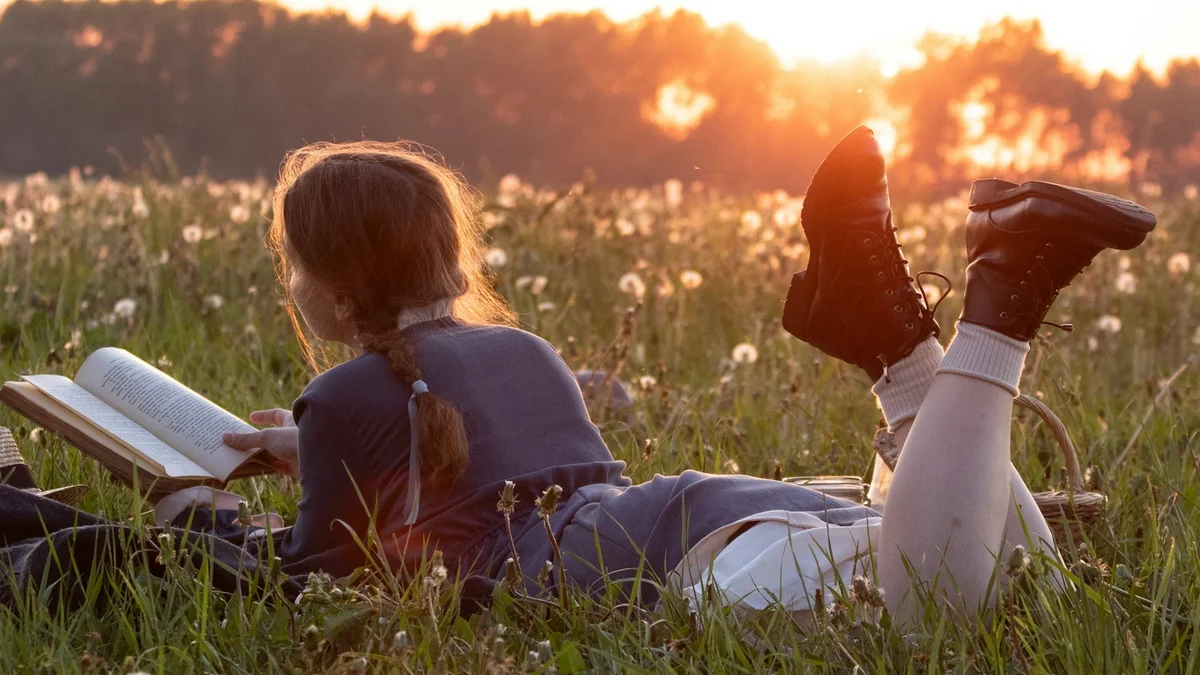 A woman lying in a wildflower meadow at sunset reading a book - a Quiet Core Reset guide to How to Give Yourself Permission to Rest.