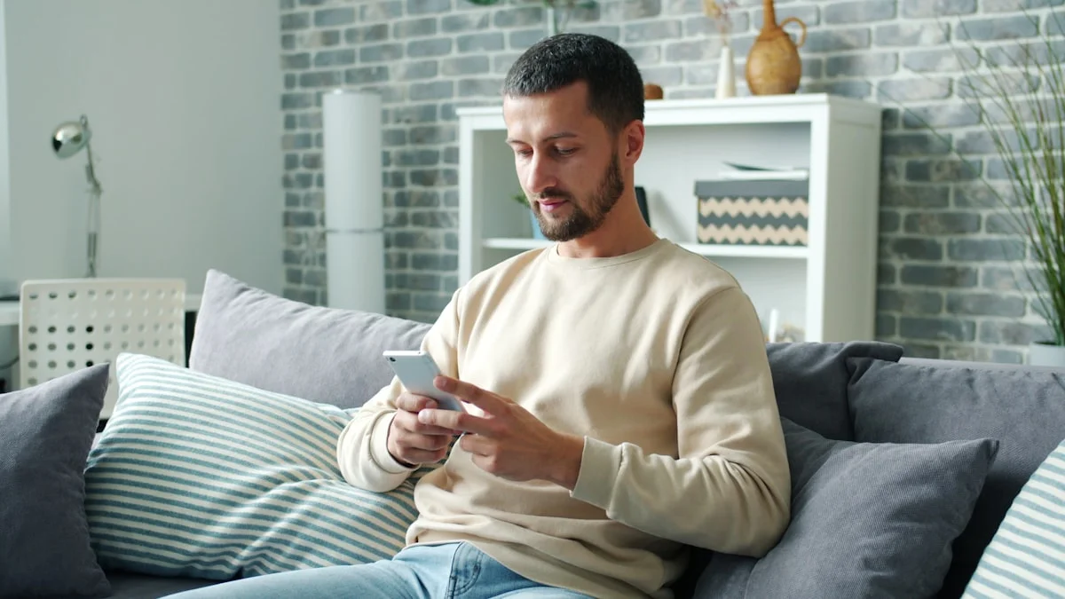 A man absorbed in his phone on a grey couch in a muted living room - a Quiet Core Reset guide to phone use and emotional flatness.