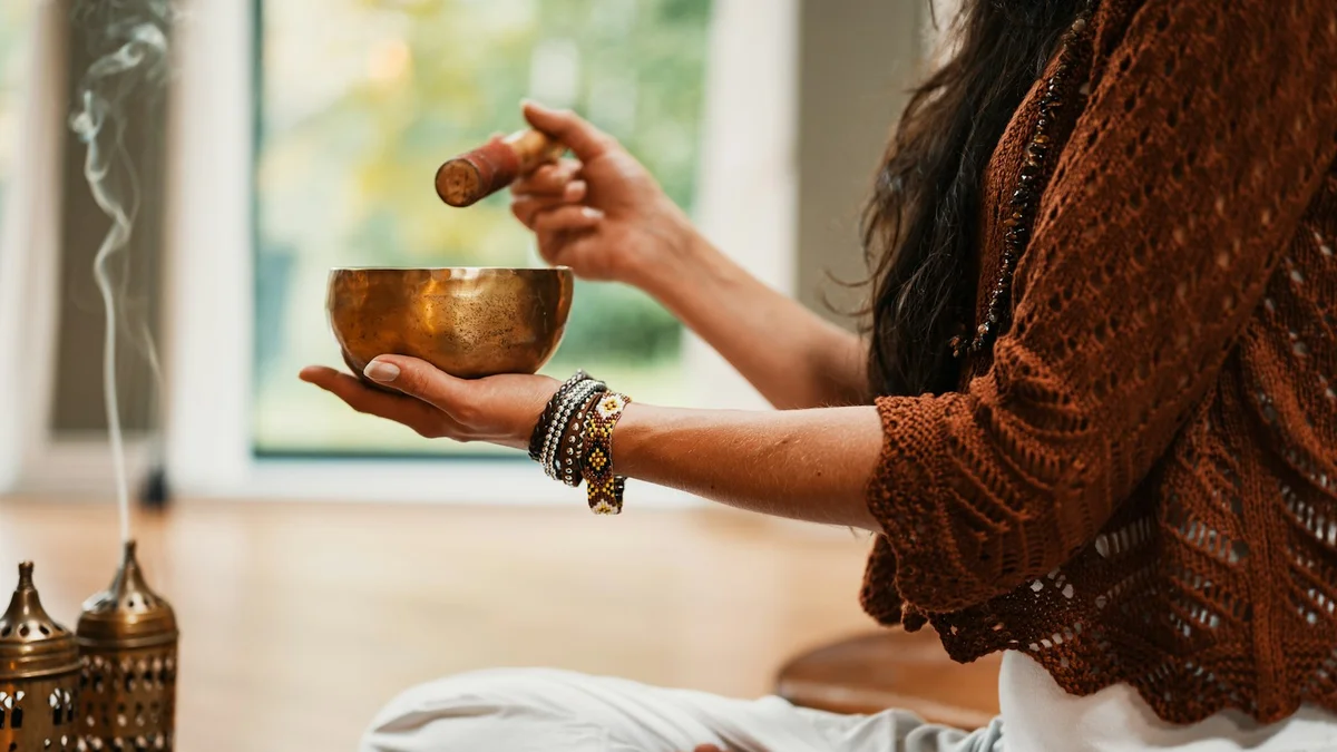 A person in a meditative pose holding a brass singing bowl, with incense smoke drifting in soft, warm light - a Quiet Core Reset guide to Physiological Sigh.