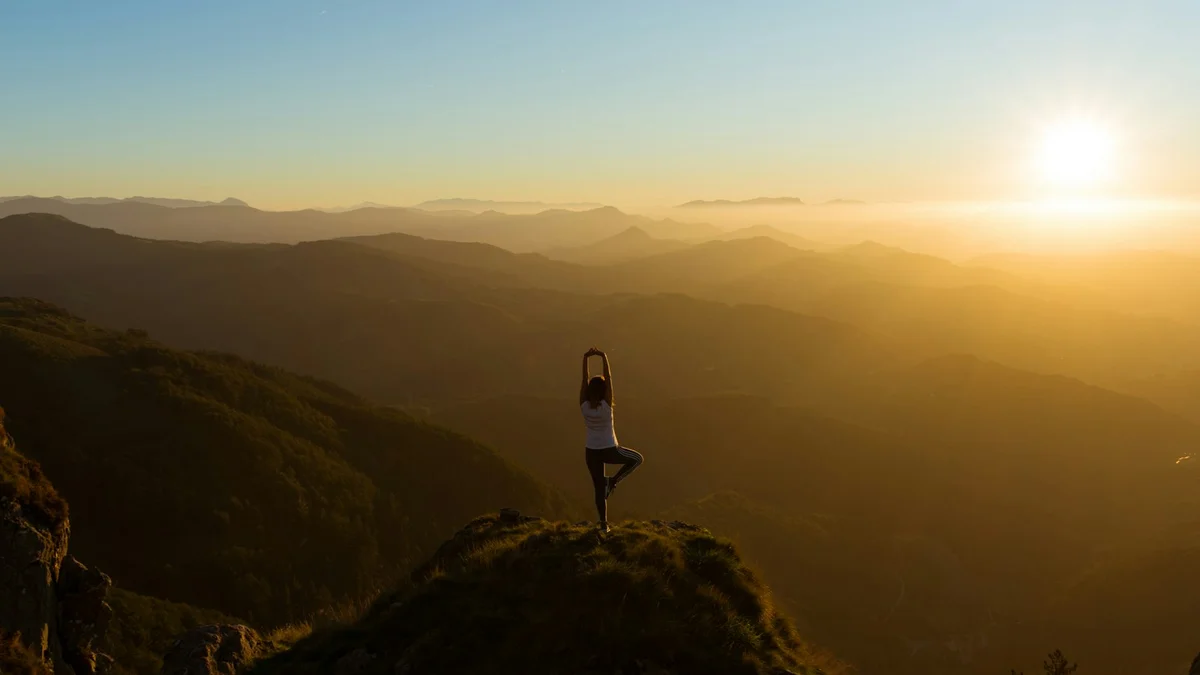 A person doing a yoga tree pose on a mountain ridge at sunrise, seen from behind against a vast golden valley - a Quiet Core Reset guide to Power of Presence.
