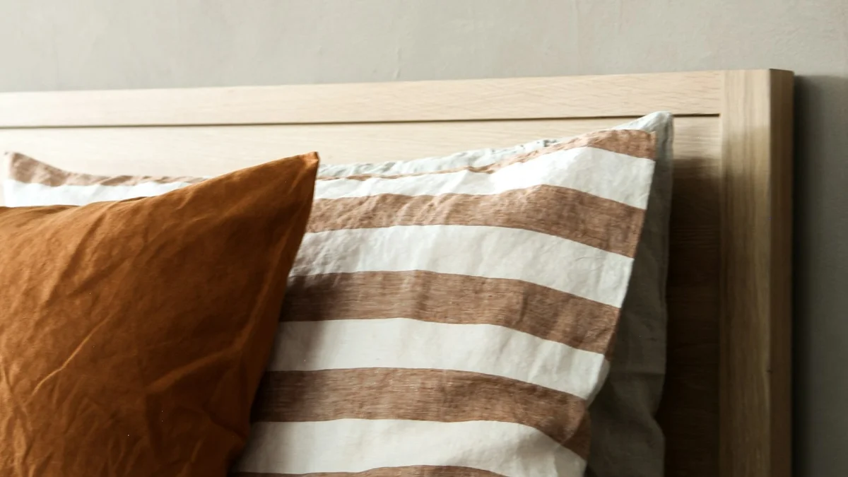 Striped linen pillows resting against a wooden headboard in soft warm light - a Quiet Core Reset guide to Pre-Sleep Body Reset.