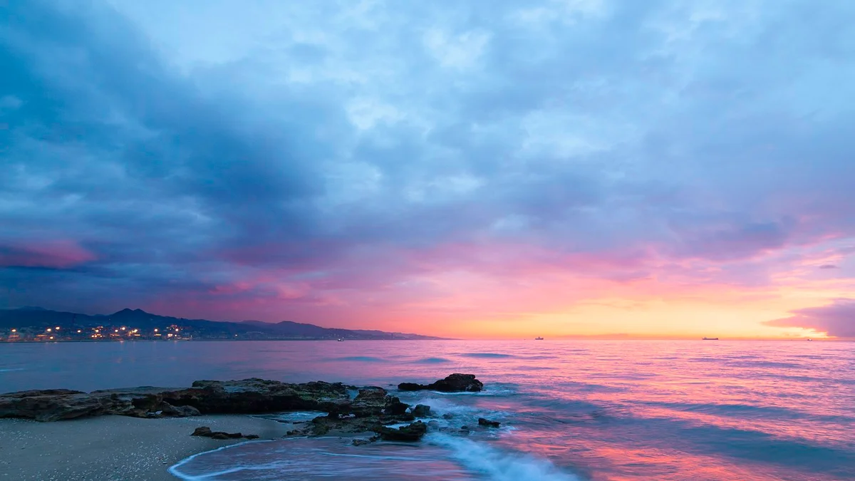 A pink and blue sunset over the ocean with rocks on the shore - a Quiet Core Reset guide to How to Protect Your Best Energy.