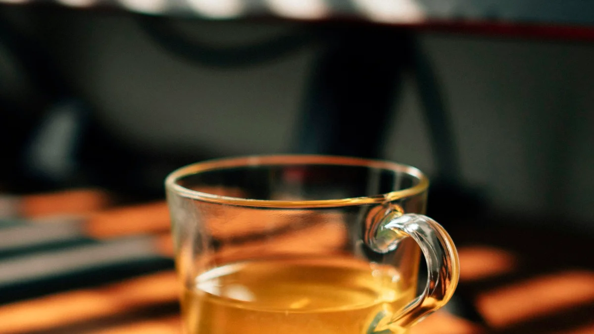 A glass cup of tea on a wooden coaster in warm light - a Quiet Core Reset guide to How to Protect Your Work Energy in 10 Minutes a Day.