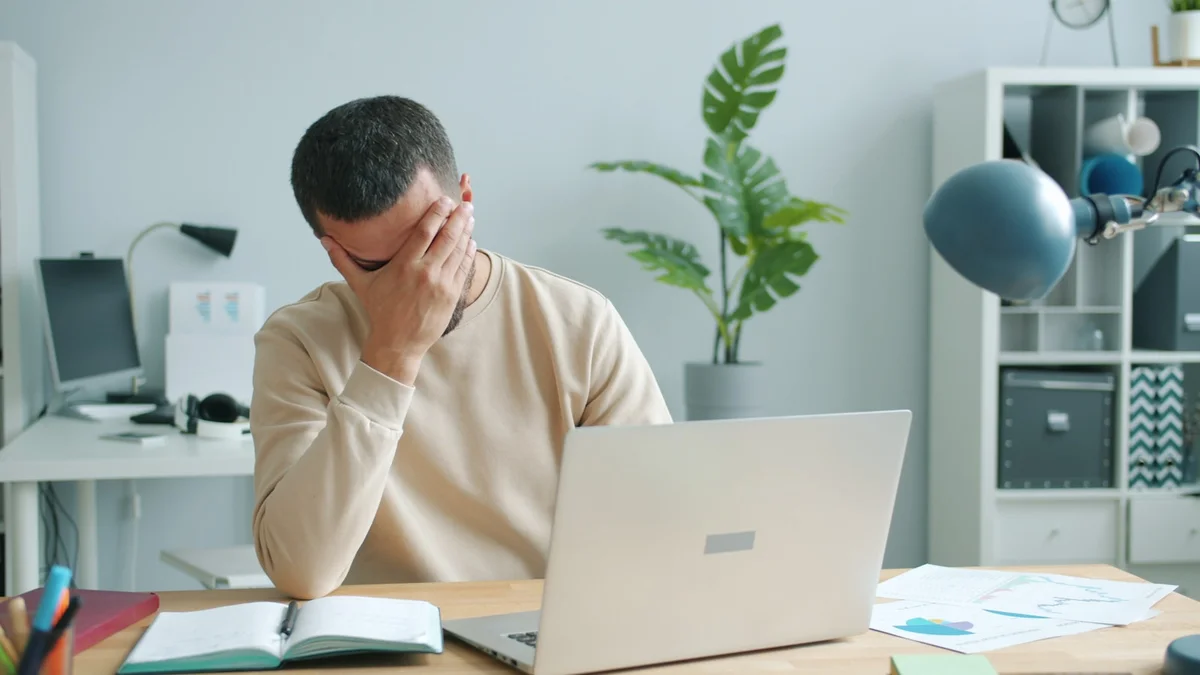 A man rubbing his eyes at a laptop in a bright home office - a Quiet Core Reset guide to Why Pushing Through the Workday Fails Your Nervous System.