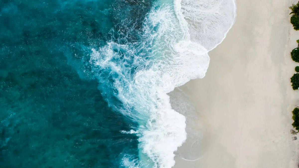 An aerial view of turquoise ocean waves breaking onto a white beach - a Quiet Core Reset guide to Why Waiting for Vacation to Recharge Doesn't Work.