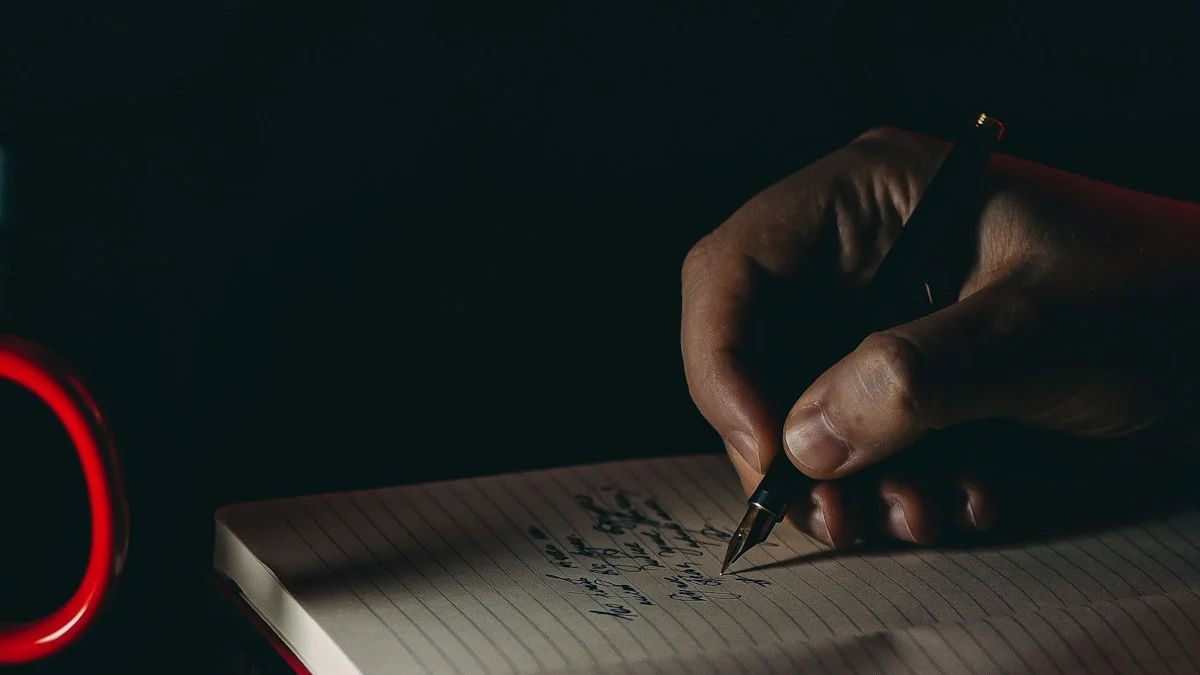 A fountain pen hand-writing in a notebook under a small pool of lamplight in a dark room - a Quiet Core Reset guide to How to Reclaim Your Focus in a Distracted World.