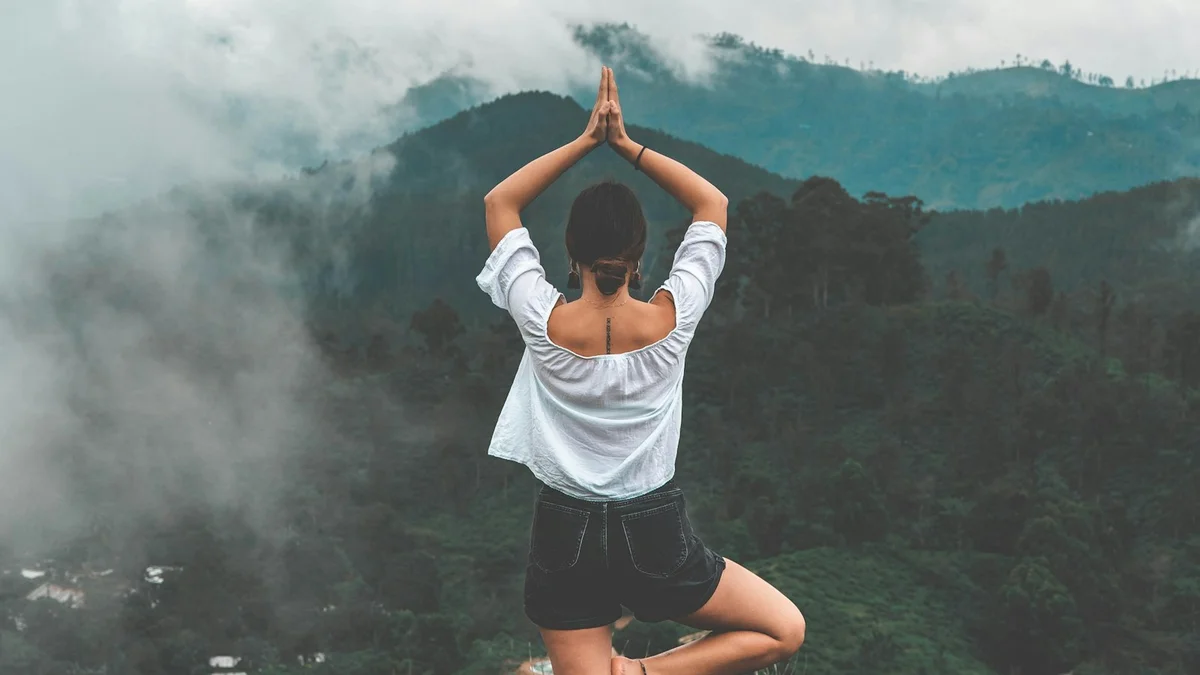 A person standing in a tree pose with hands pressed together above their head, overlooking misty green mountains - a Quiet Core Reset guide to Replenish Through Presence.