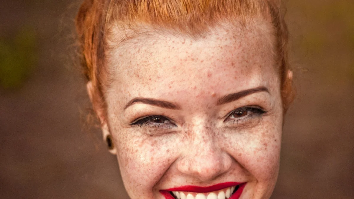 A close-up portrait of a smiling freckled woman with red hair and red lipstick - a Quiet Core Reset guide to Resetting Your Expectations.