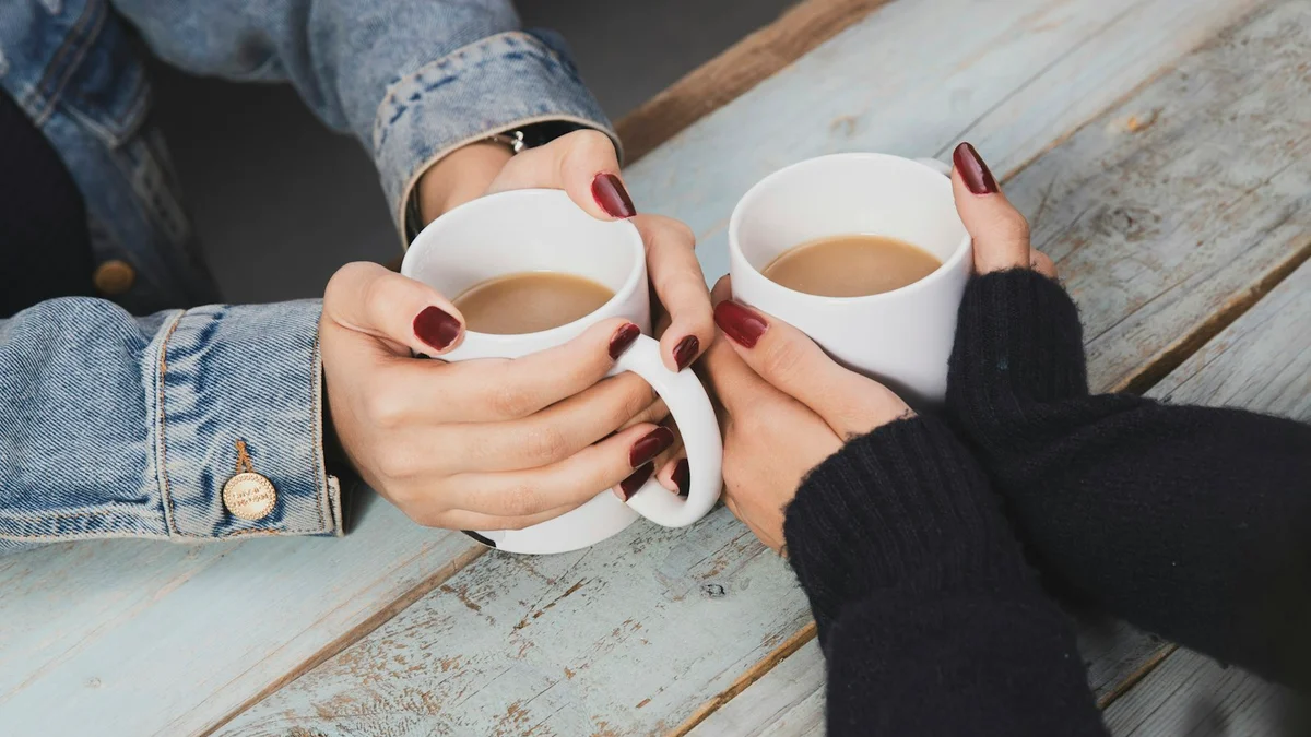 Two pairs of hands holding warm mugs together over a wooden table - a Quiet Core Reset guide to Rest Guilt for Caregivers.