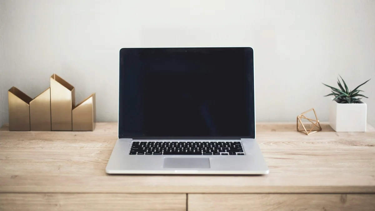 A dark-screen laptop resting on a tidy wooden desk beside a small plant - a Quiet Core Reset guide to Rest Guilt for High Achievers.