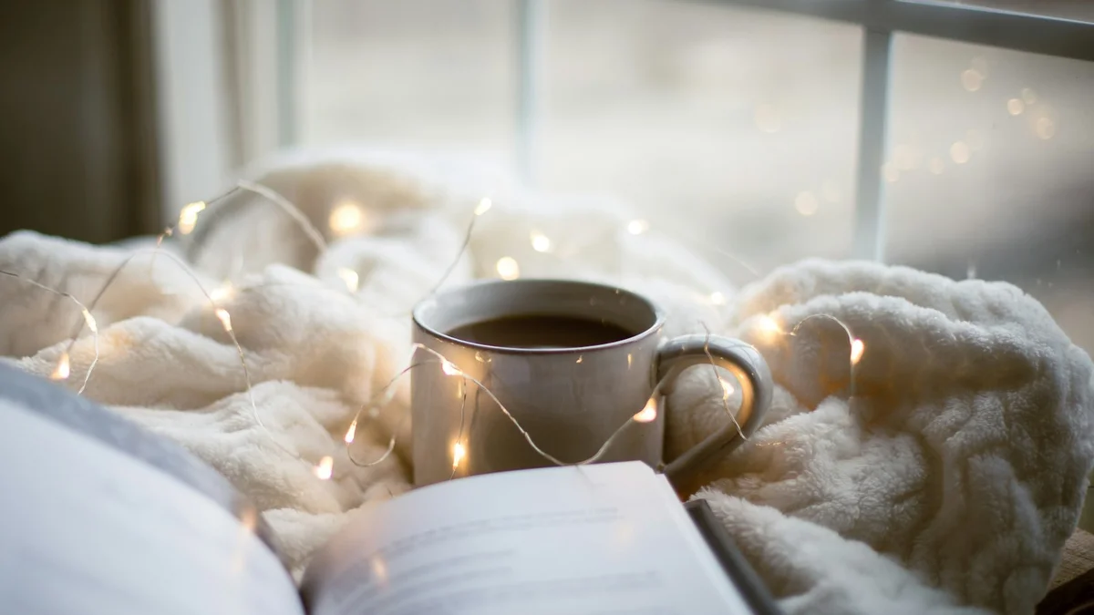 An open book and a warm mug on a cream blanket beside a bright window - a Quiet Core Reset guide to 5 Myths About Rest Guilt That Keep You Exhausted.