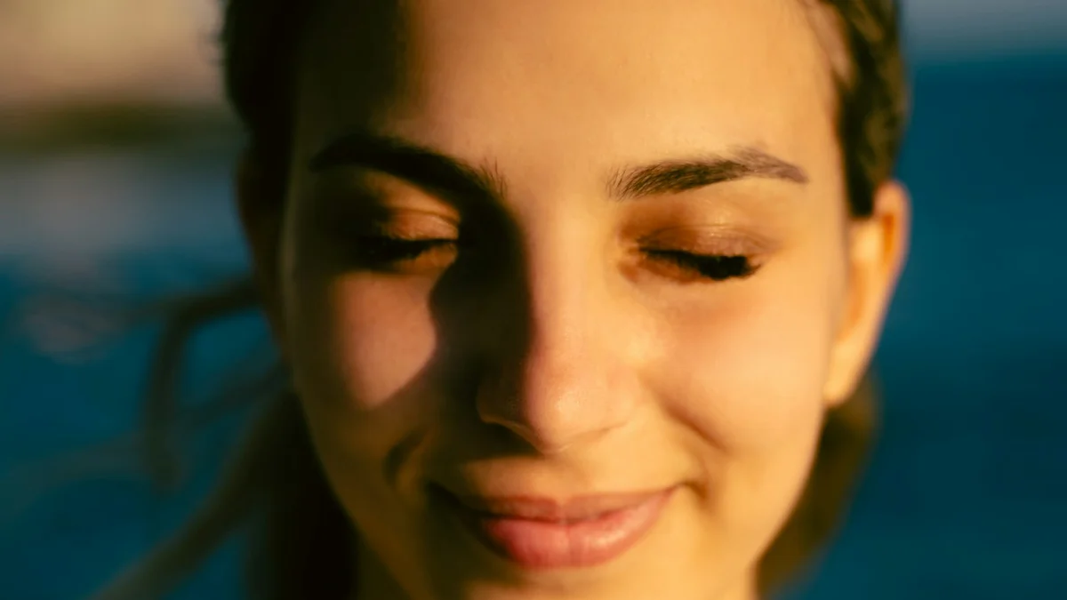 A woman with her eyes closed smiling softly in warm golden light - a Quiet Core Reset guide to The Science of Rest Guilt.
