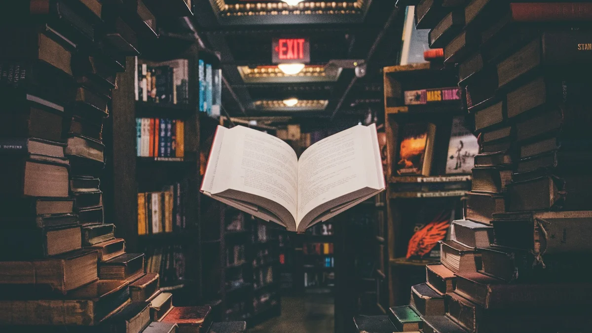 An open book floating between tall stacks of books in a dim library or bookshop - a Quiet Core Reset guide to Rest Is Productive.