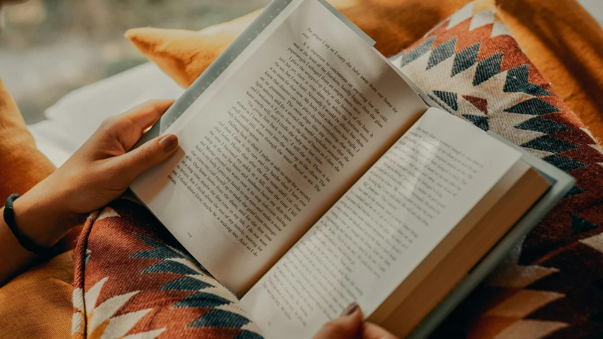 Hands holding an open book under a soft warm blanket - a Quiet Core Reset guide to Rest vs. Laziness.
