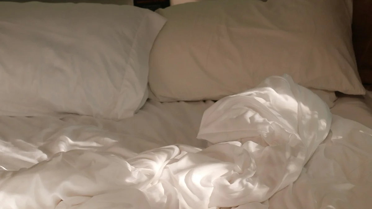 A rumpled white bed with soft pillows in warm afternoon sunlight - a Quiet Core Reset guide to Resting on Low-Energy Days Without the Guilt Spiral.