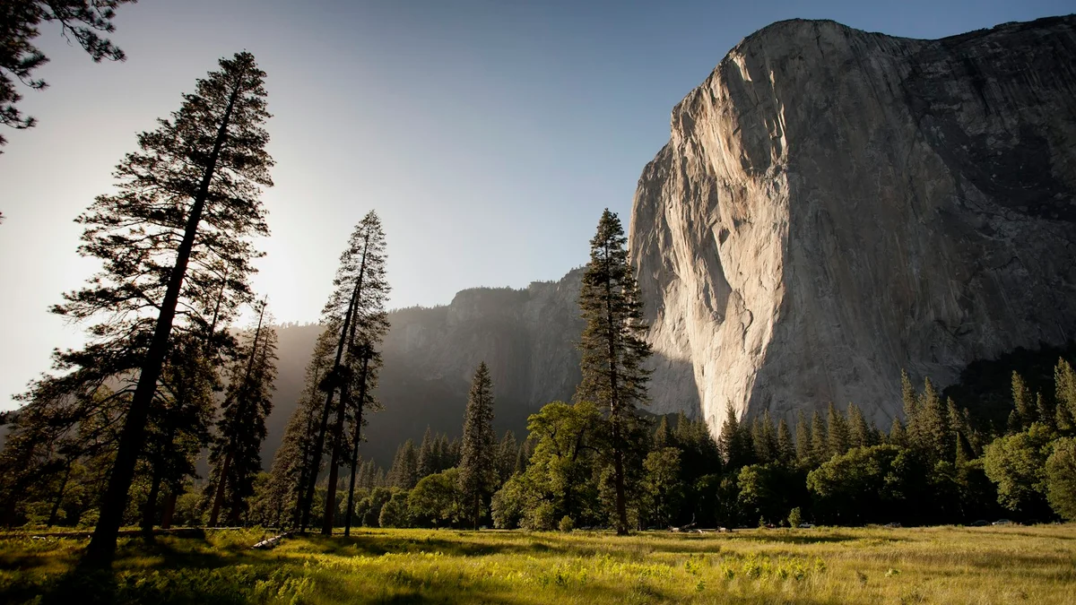 A huge granite rock face rising above a meadow with pine trees and warm light - a Quiet Core Reset guide to How to Restore Your Energy Without a Vacation.