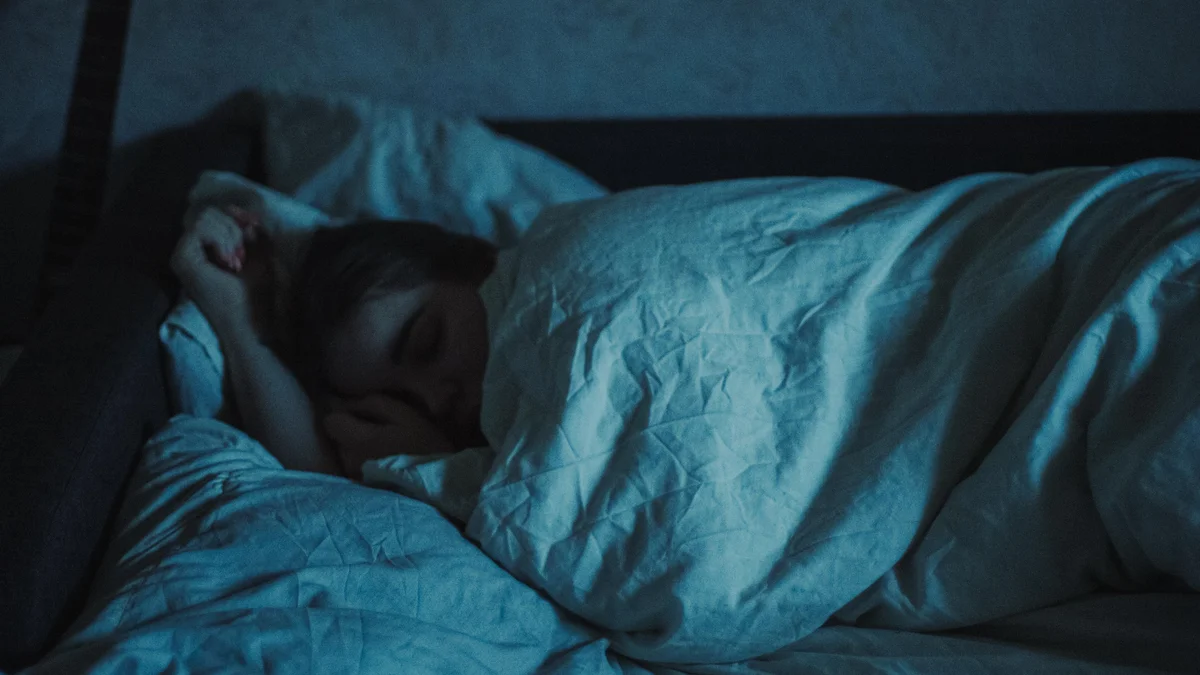A person asleep under a white duvet in a dim blue-toned bedroom at night - a Quiet Core Reset guide to 9 Signs You're Asleep but Not Actually Recovering.