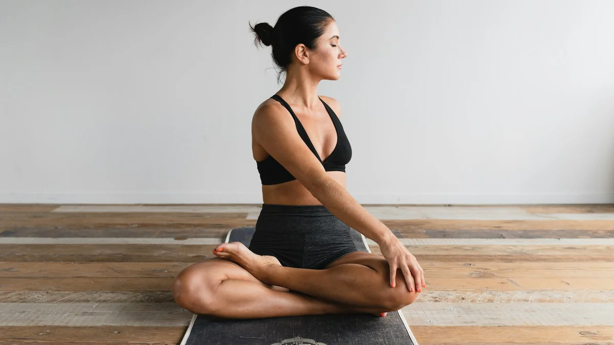 A woman meditating cross-legged on a yoga mat on a wooden floor, eyes closed, calm - a Quiet Core Reset guide to 8 Signs Your Breathing Is Keeping You Stressed.