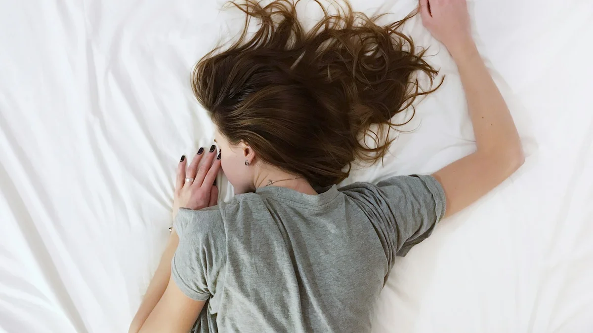 A person lying face down on a white bed, exhausted - a Quiet Core Reset guide to Sleep Recovery When You're Already Burned Out.
