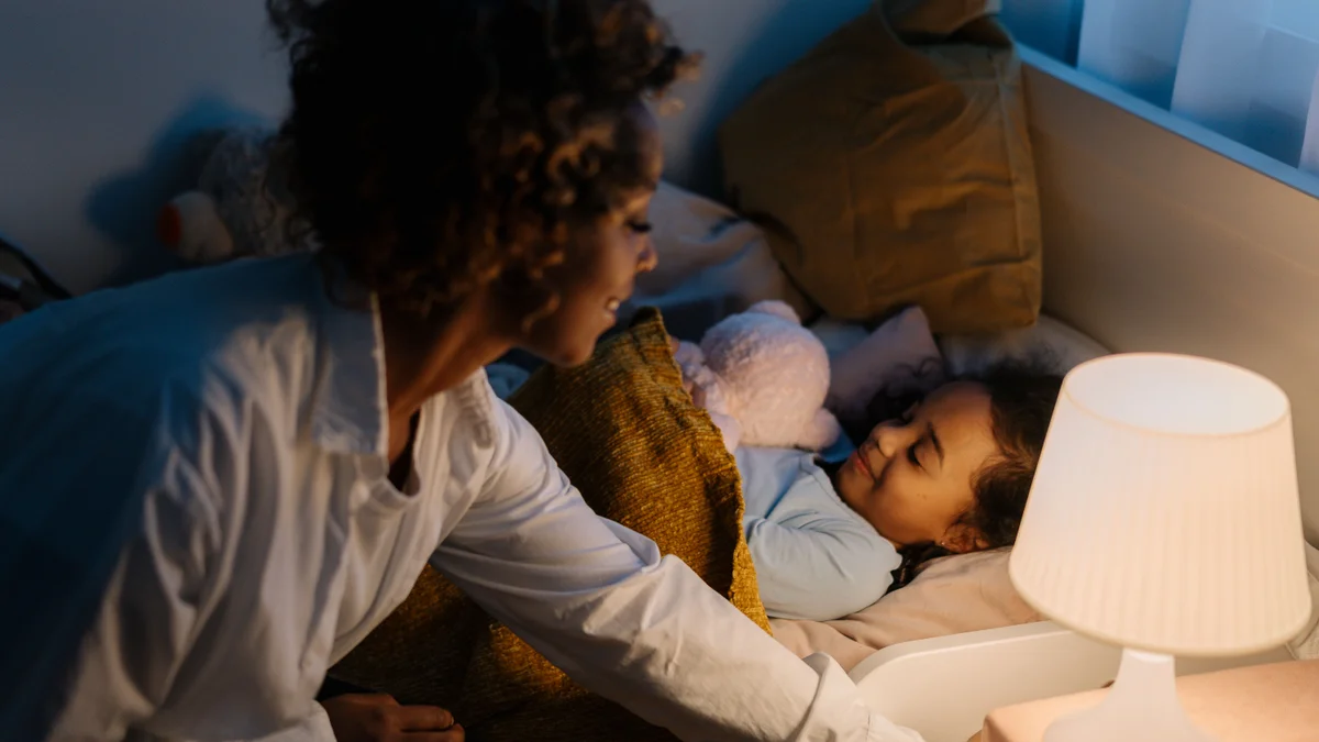 A parent tucking a child into bed at night beside a softly glowing lamp - a Quiet Core Reset guide to Sleep Recovery for Parents.