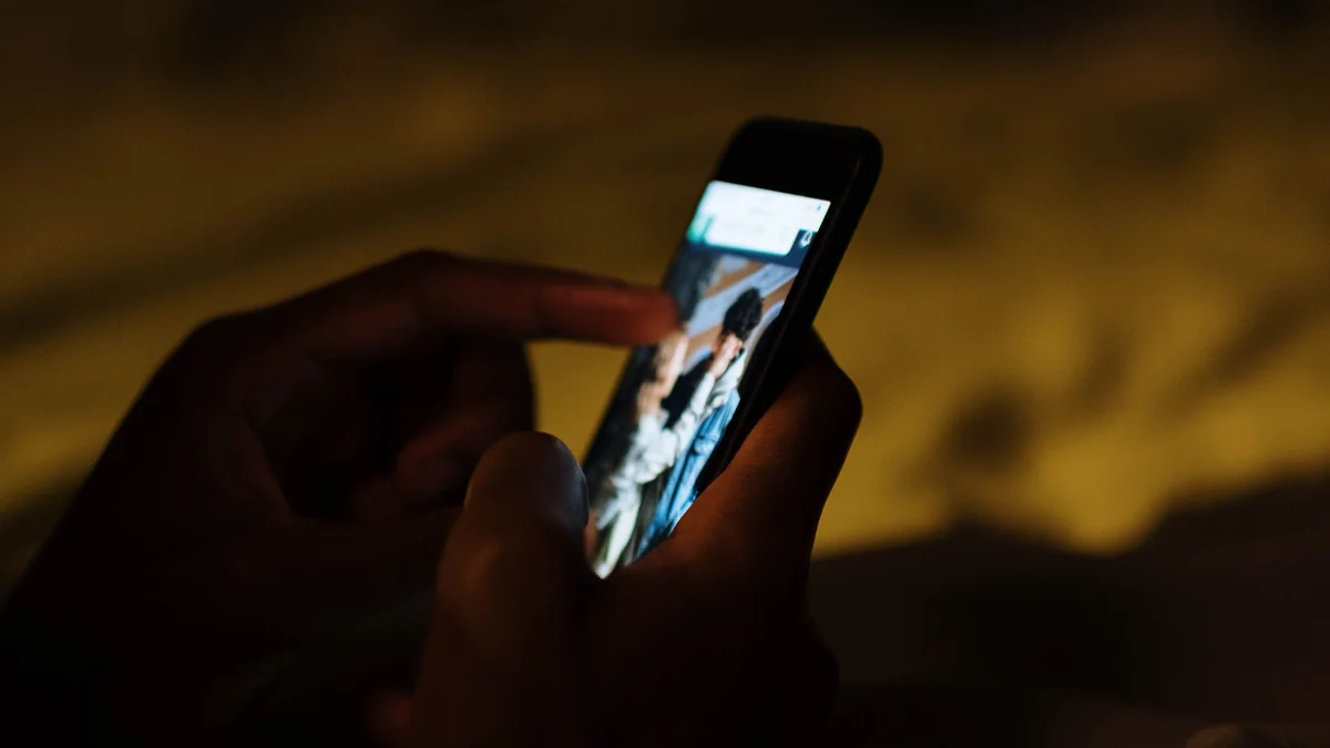 A hand scrolling a glowing phone in a dark bedroom at night - a Quiet Core Reset guide to 9 Sleep Recovery Mistakes (and the Gentler Fix for Each).