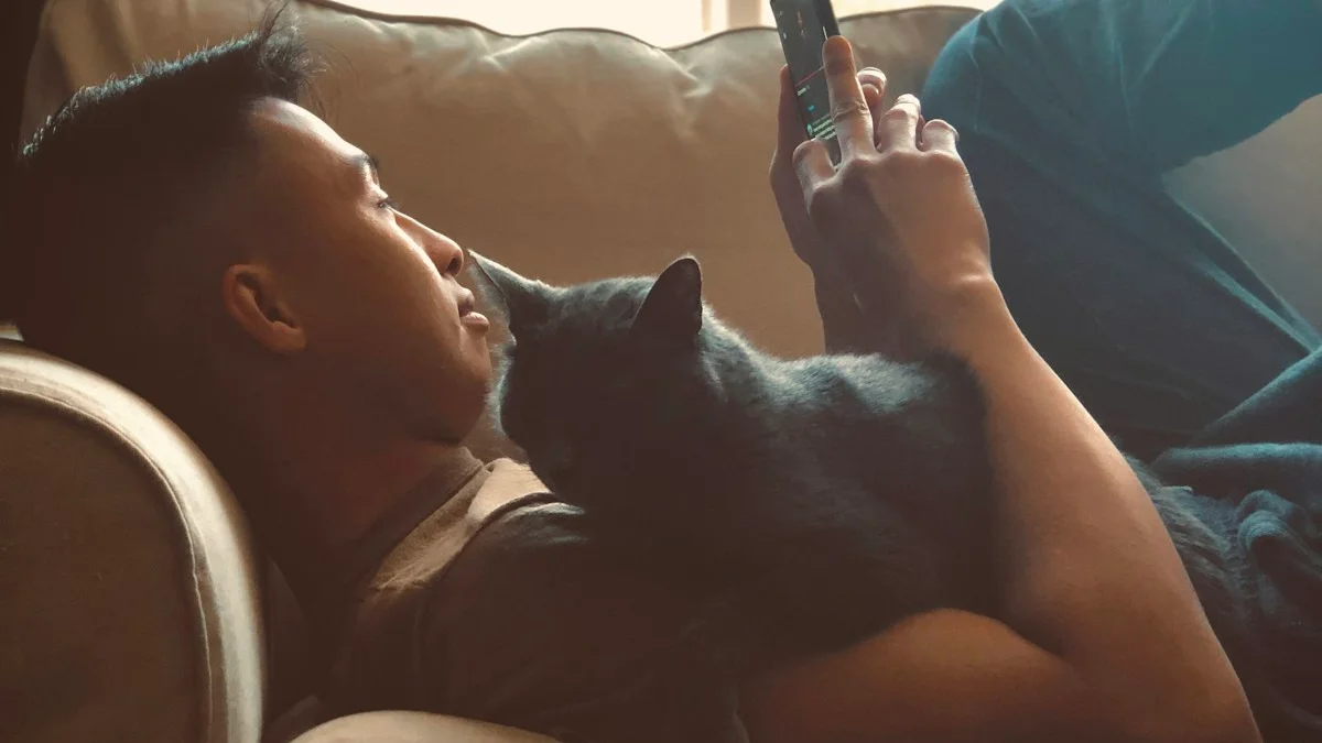 A man recharging alone on the couch with a cat on his chest, phone in hand in soft window light - a Quiet Core Reset guide to Social Battery.
