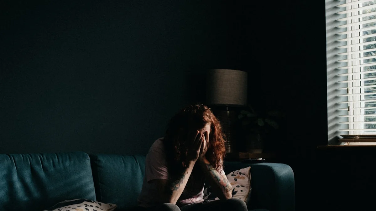 A person sitting on a dark sofa in a dim living room at night, hands pressed to their face - a Quiet Core Reset guide to Social Comparison and Stress Hormones.