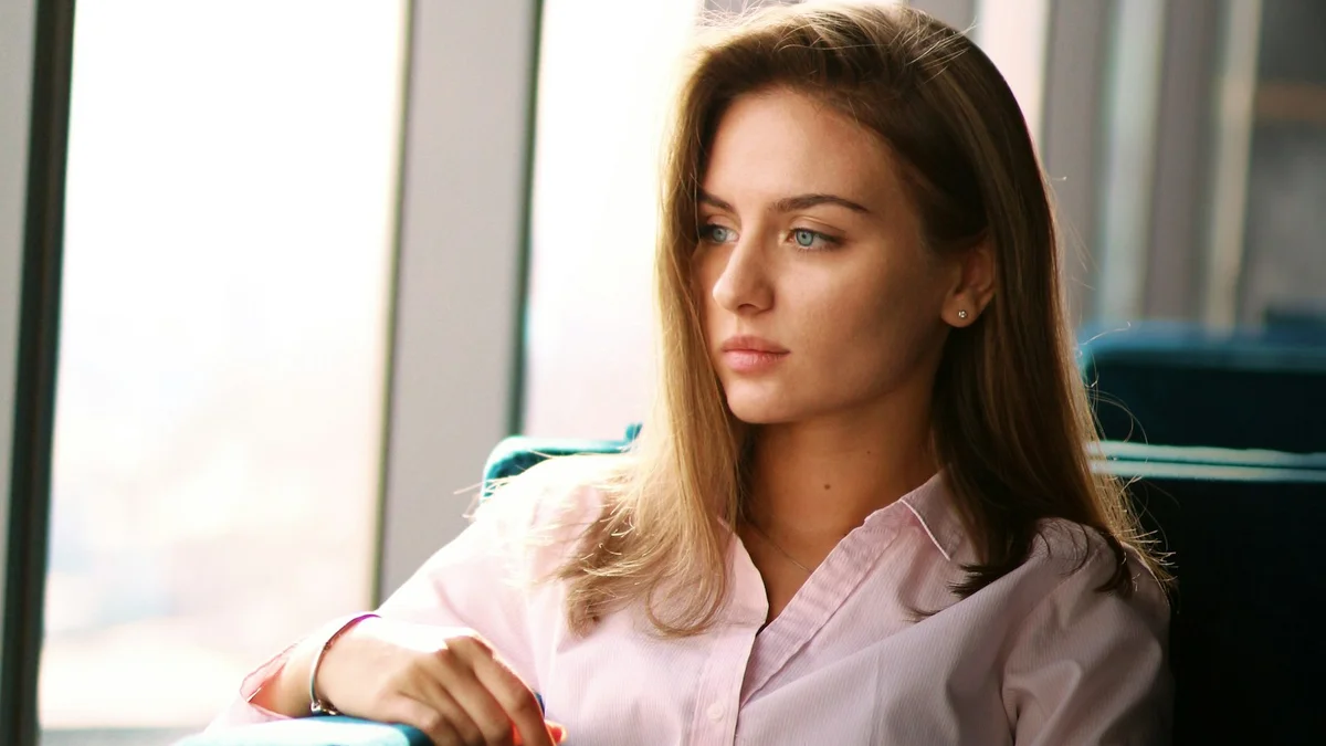 A professional sitting quietly by large office windows, looking away in thought - a Quiet Core Reset guide to Subtle Signs Your Work Energy Is Draining (That Look Normal).