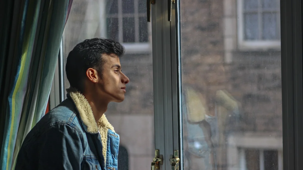 A young man in a denim jacket gazes out a sunlit window, quiet and pensive - a Quiet Core Reset guide to Why Just Think Positive Doesn't Work.