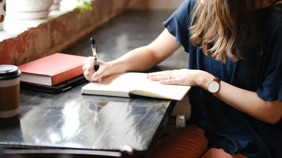 A woman writing in an open notebook at a table with a coffee cup and books - a Quiet Core Reset guide to Tired or Depleted? The Printable Self-Check.