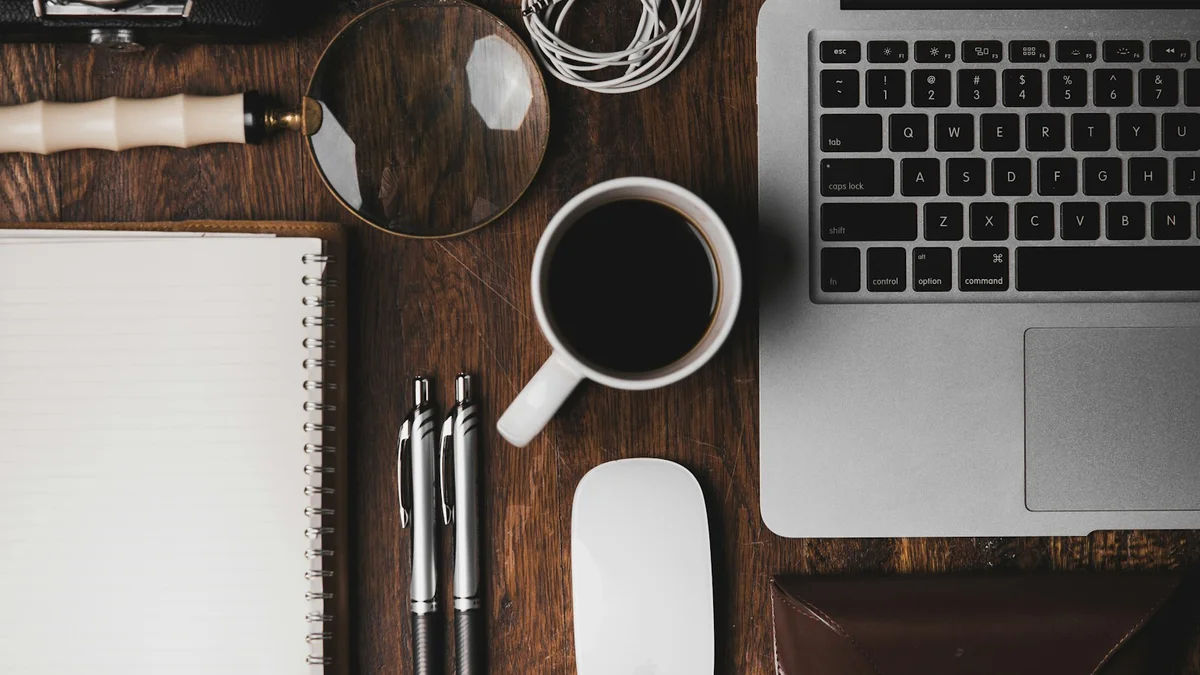 A flat-lay desk with a notebook, coffee, pens, a magnifying glass and a laptop on wood - a Quiet Core Reset guide to Why 'I Don't Have Time for a Break' Is Now the Default.