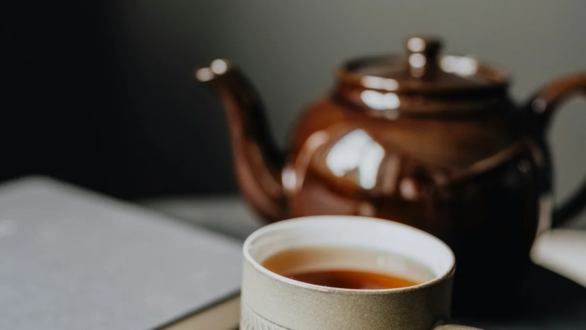 A ceramic mug of tea beside a teapot and a closed notebook on a wooden table - a Quiet Core Reset guide to How to Unlearn Rest Guilt in 10 Minutes a Day.