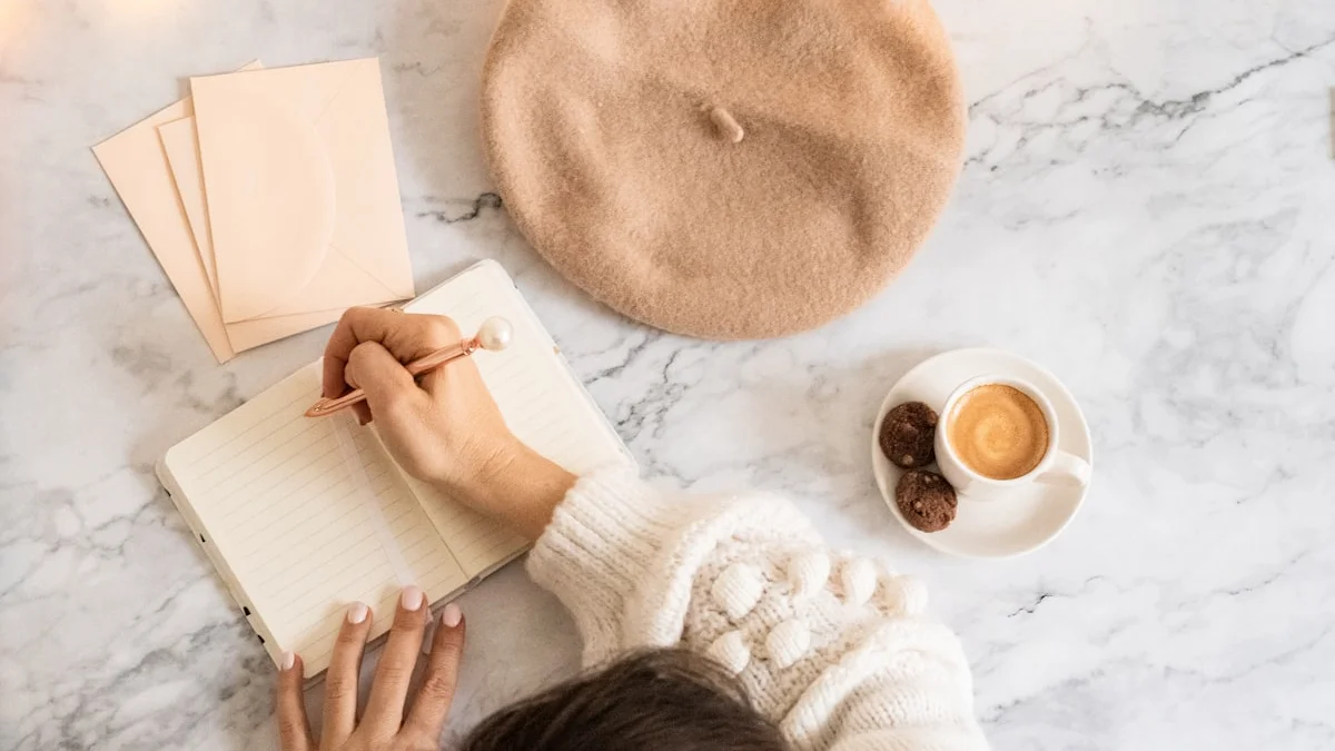 A hand writing in an open notebook beside a beret, espresso, and soft fairy lights on a marble table - a Quiet Core Reset guide to Unlearning Hustle Culture: Step by Step (Exact Instructions).