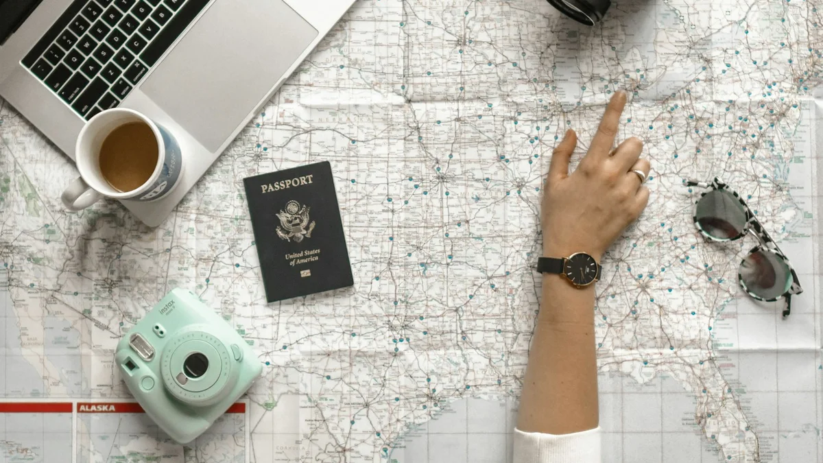 A hand pointing at a map with a passport, camera, coffee and sunglasses on a travel planning desk - a Quiet Core Reset guide to Why Waiting for Big Moments Keeps You Stuck.
