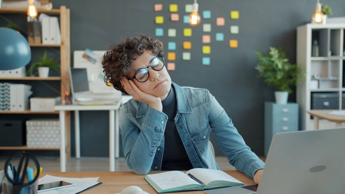 A woman at her office desk propping her head in one hand, eyes closed amid sticky notes and open work - a Quiet Core Reset guide to What Is High-Functioning Exhaustion?
