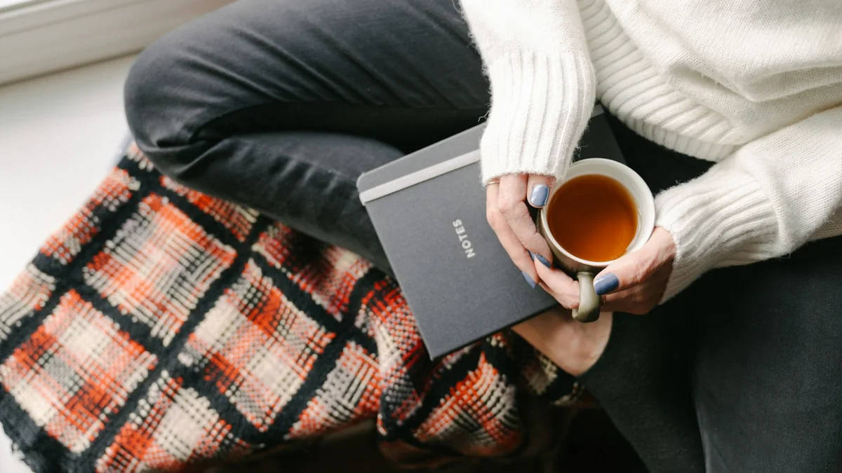 A person sitting on a window seat holding a warm mug of tea beside a notebook - a Quiet Core Reset guide to What Is Rest Guilt? The Belief That Rest Must Be Earned.