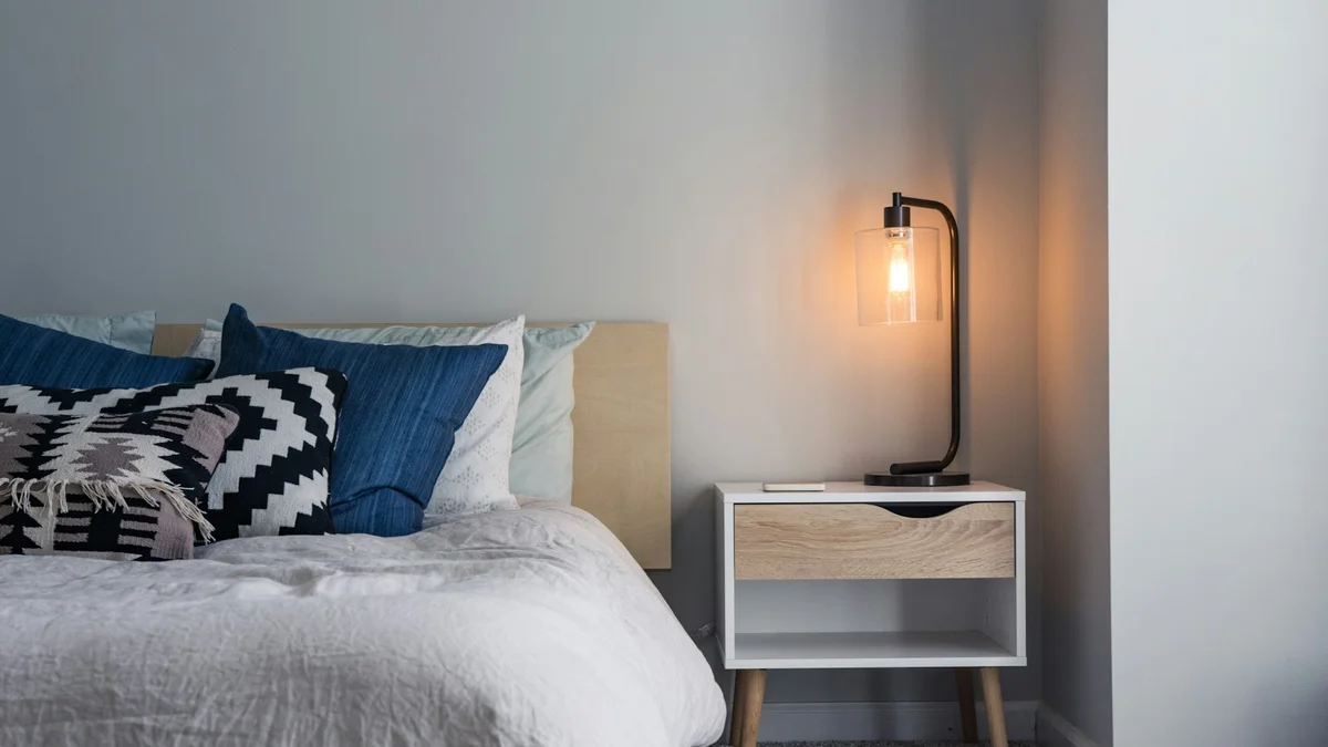 A calm bedroom at dusk with a warm lamp glowing beside blue pillows and soft bedding - a Quiet Core Reset guide to What Is Sleep Recovery? A Nervous-System Definition.