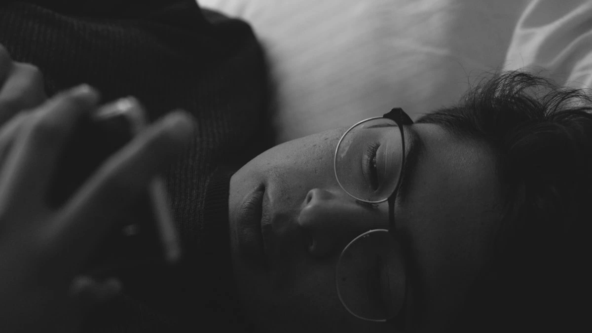 A weary person lying in bed at dawn looking at a glowing phone, soft black-and-white light - a Quiet Core Reset guide to What Is Social Comparison Fatigue.