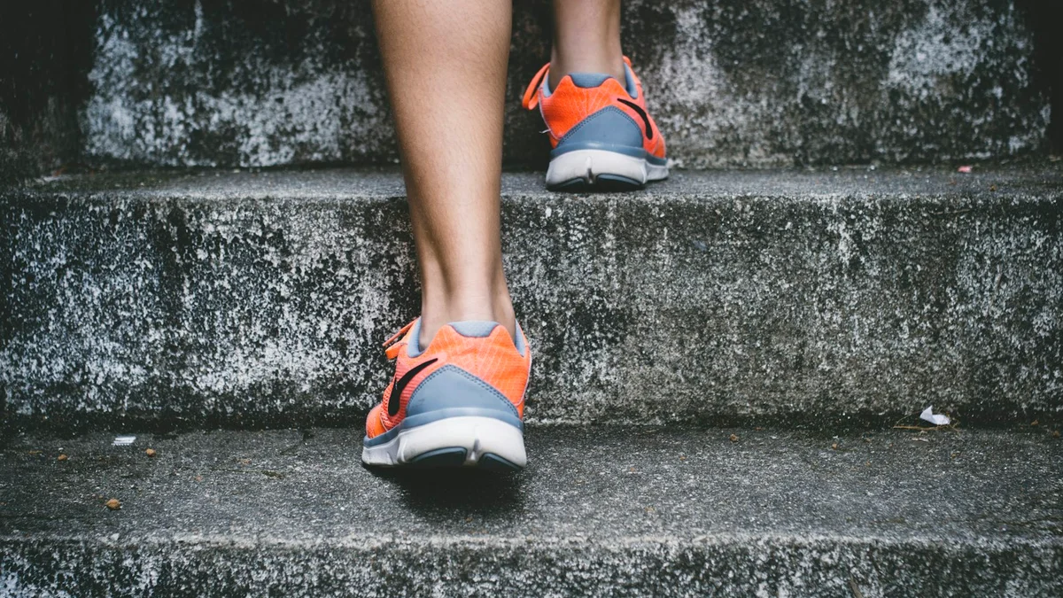 A person's feet in orange running shoes stepping up grey concrete stairs - a Quiet Core Reset guide to When Your Body Starts Shouting.