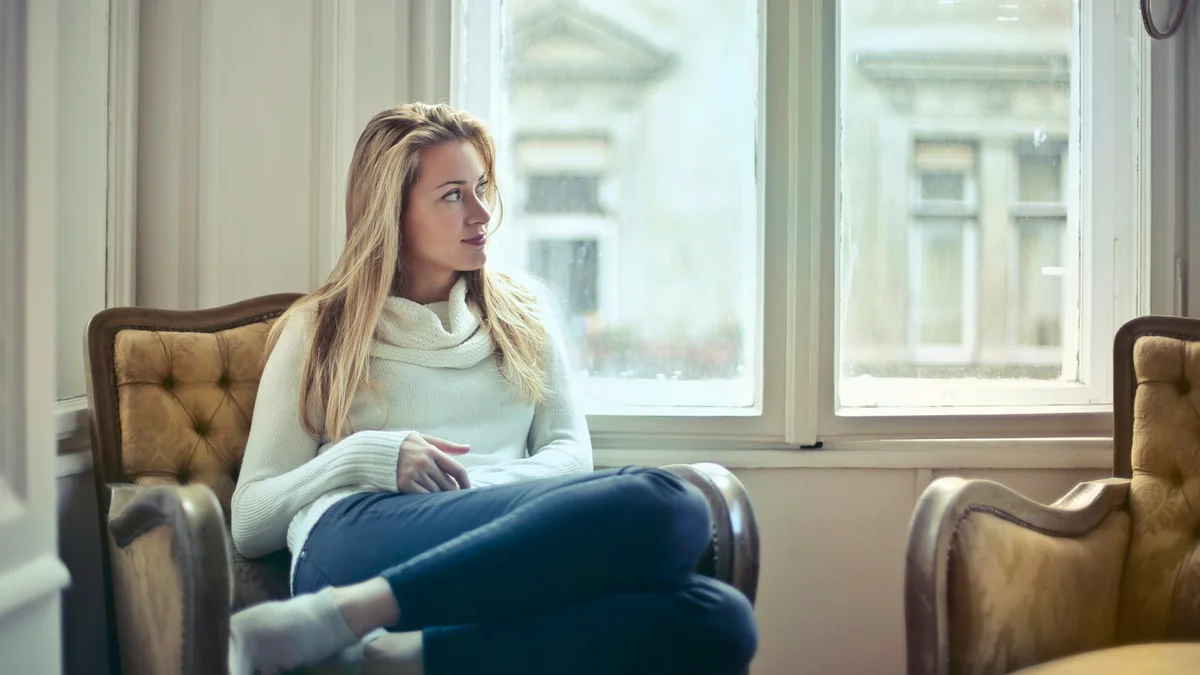 A woman curled up with her thoughts in an armchair by a bright window - a Quiet Core Reset guide to Why Do I Feel Guilty When I Rest? 6 Real Causes.