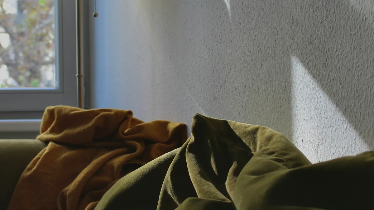 A cozy couch draped with soft blankets beside a bright sunlit window - a Quiet Core Reset guide to Why Rest Guilt Is So Common Now (It's Not Just You).