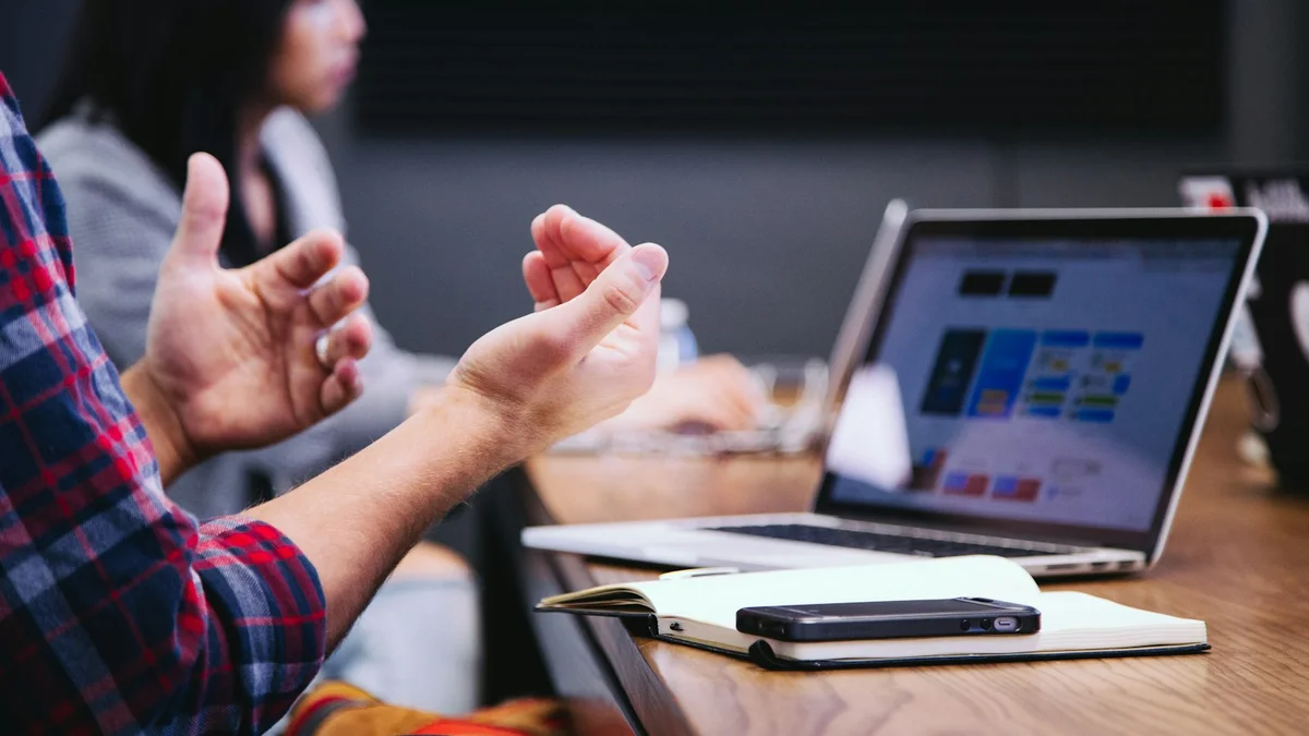 Two people talking and gesturing in a meeting with a laptop and notebook on the table - a Quiet Core Reset guide to Why Routines Fail.