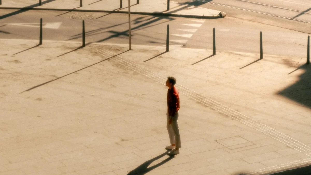 A single person standing in a wide sunlit city square - a Quiet Core Reset guide to Why Self-Criticism Feels Normal Right Now (It's the Culture).