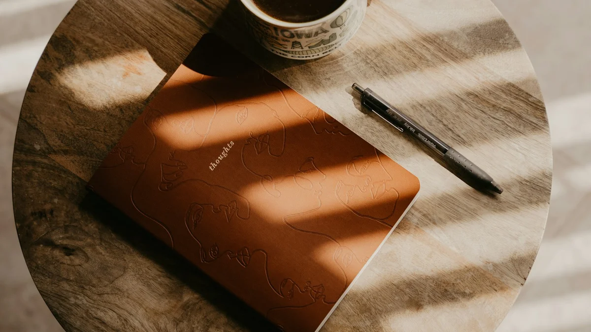 A notebook, pen, and cup of coffee on a round wooden table in striped morning light - a Quiet Core Reset guide to How Much Work Energy Do You Have Left? A 5-Minute Self-Check.