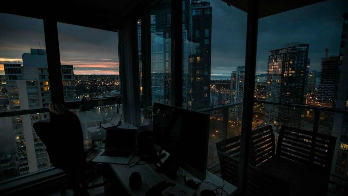 A darkened desk at dusk with city lights outside the window - a Quiet Core Reset guide to Working While Burned Out.