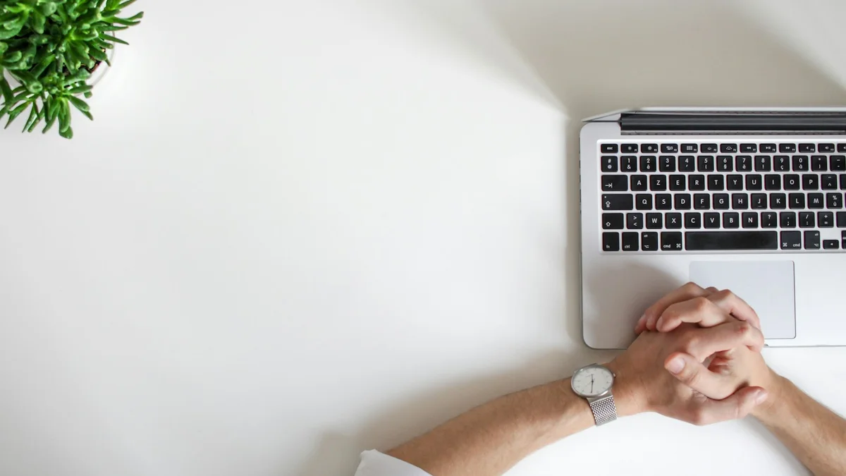 Clasped hands resting in front of a closed laptop on a white desk - a Quiet Core Reset guide to 7 Subtle Signs Your Worth Is Tied to Your Output.